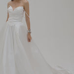 Bride wearing a duchess satin basque waist wedding dress on a plain white backdrop